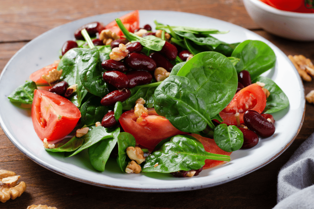 red bean salad, vegan salas with spinach, cherry tomatoes, walnuts, beans, mustard dressing on wooden background