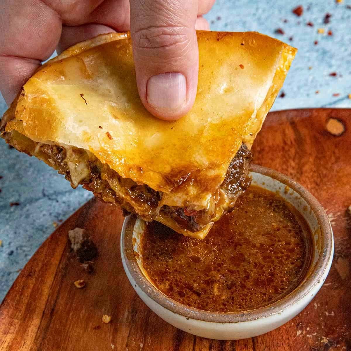 Birria quesadilla being dipped into a cup of consomé