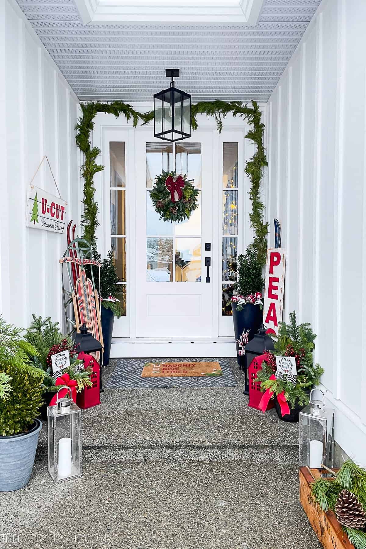 Modern farmhouse Christmas porch in red, black and white with evergreen pots and a live wreath