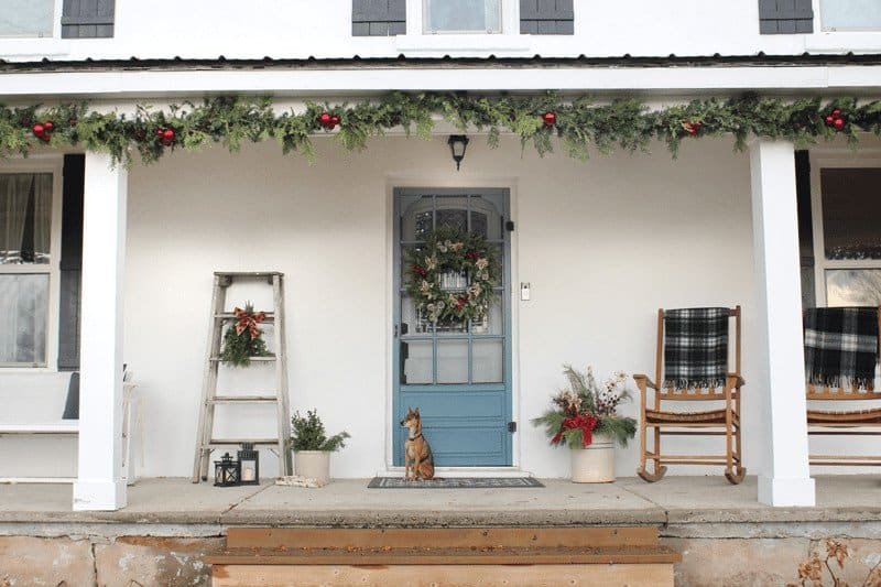 Old fashioned farmhouse Christmas porch with evergreen garland, rocking chairs and tartan blankets