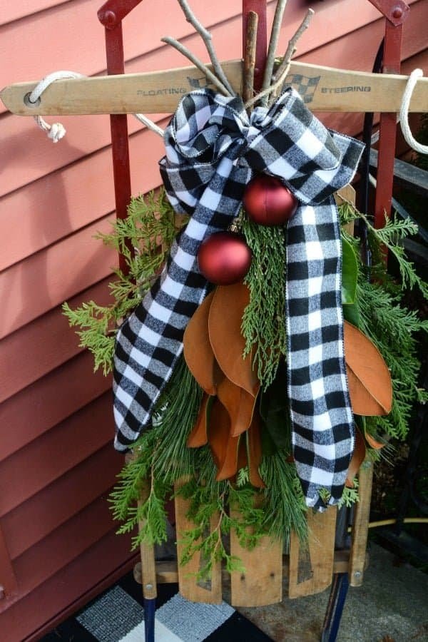 Vintage wooden sled decorated with a cedar, pine and magnolia bough, plaid ribbon and red ornaments