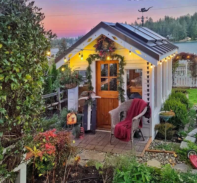 Small Christmas porch with string lights, fresh garland and a cozy chair at sunset