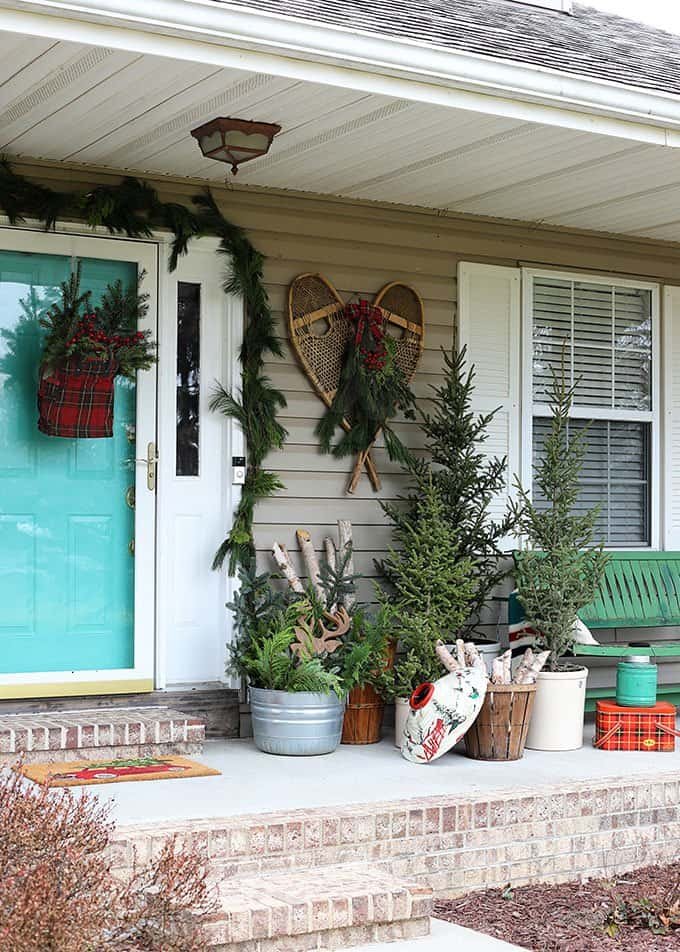 Vintage lodge Christmas porch with snowshoes, plaid blanket and evergreen tree tops in crocks
