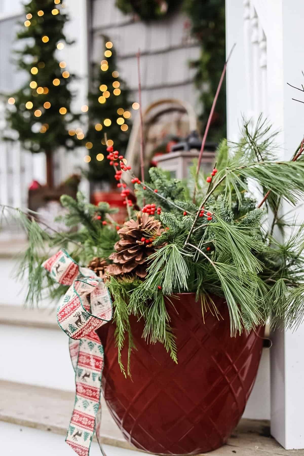 Vintage red and green Christmas porch with mini trees and a red planter filled with winterberries