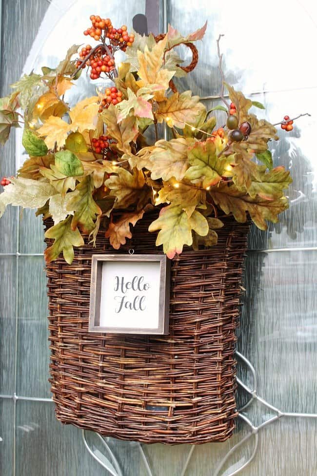 DIY fall basket wreath filled with faux leaves, a hello fall sign and twinkle lights on the front door