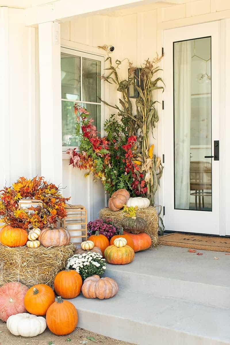 Tall corn stalks tied with twine to porch posts alongside Indian corn and pumpkins