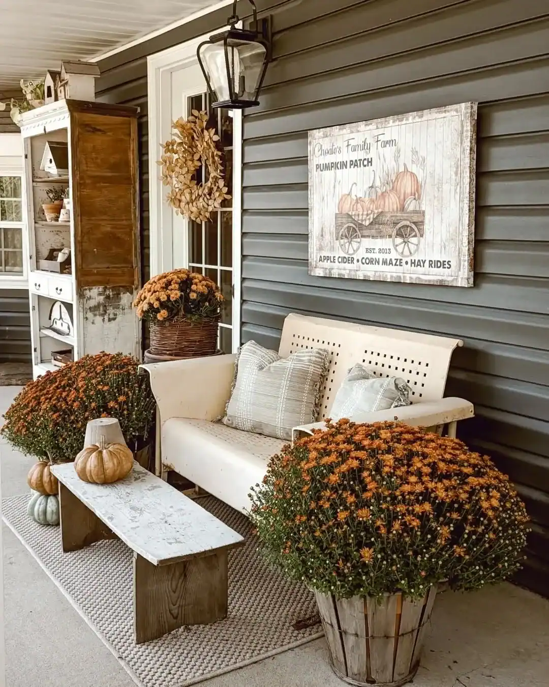 Dark charcoal siding behind a farmhouse fall porch display with pumpkins, mums and a vintage bench