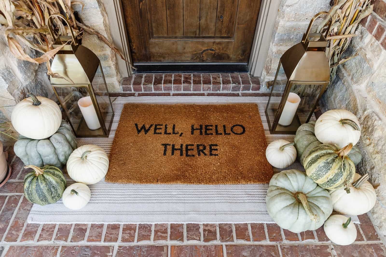 Stenciled fall doormat layered over a neutral striped outdoor rug on a front porch