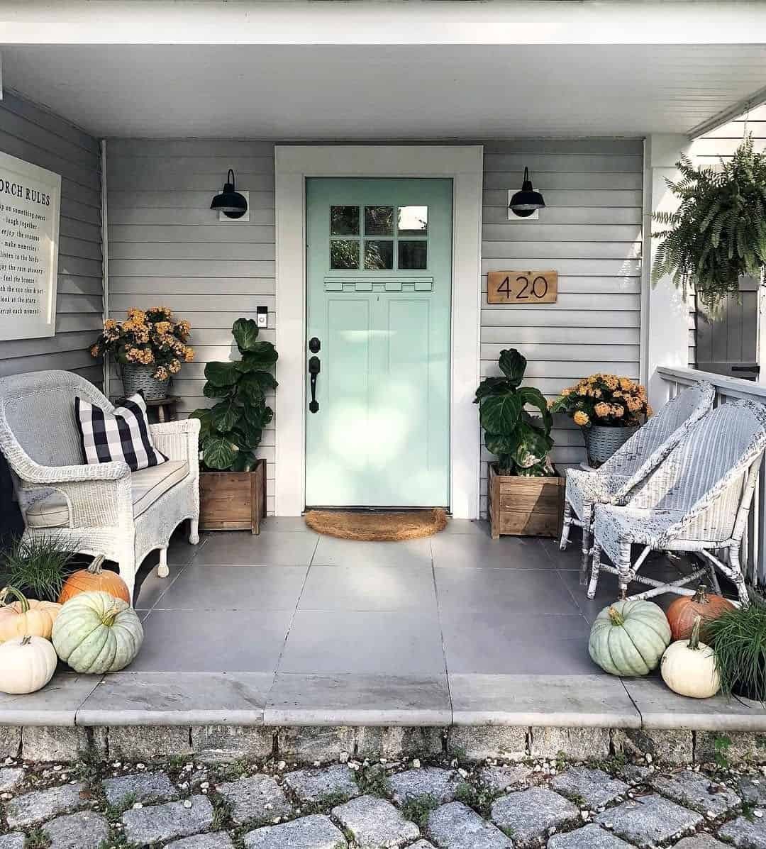 Pale mint front door against gray siding with white wicker seating and pumpkins set on the floor