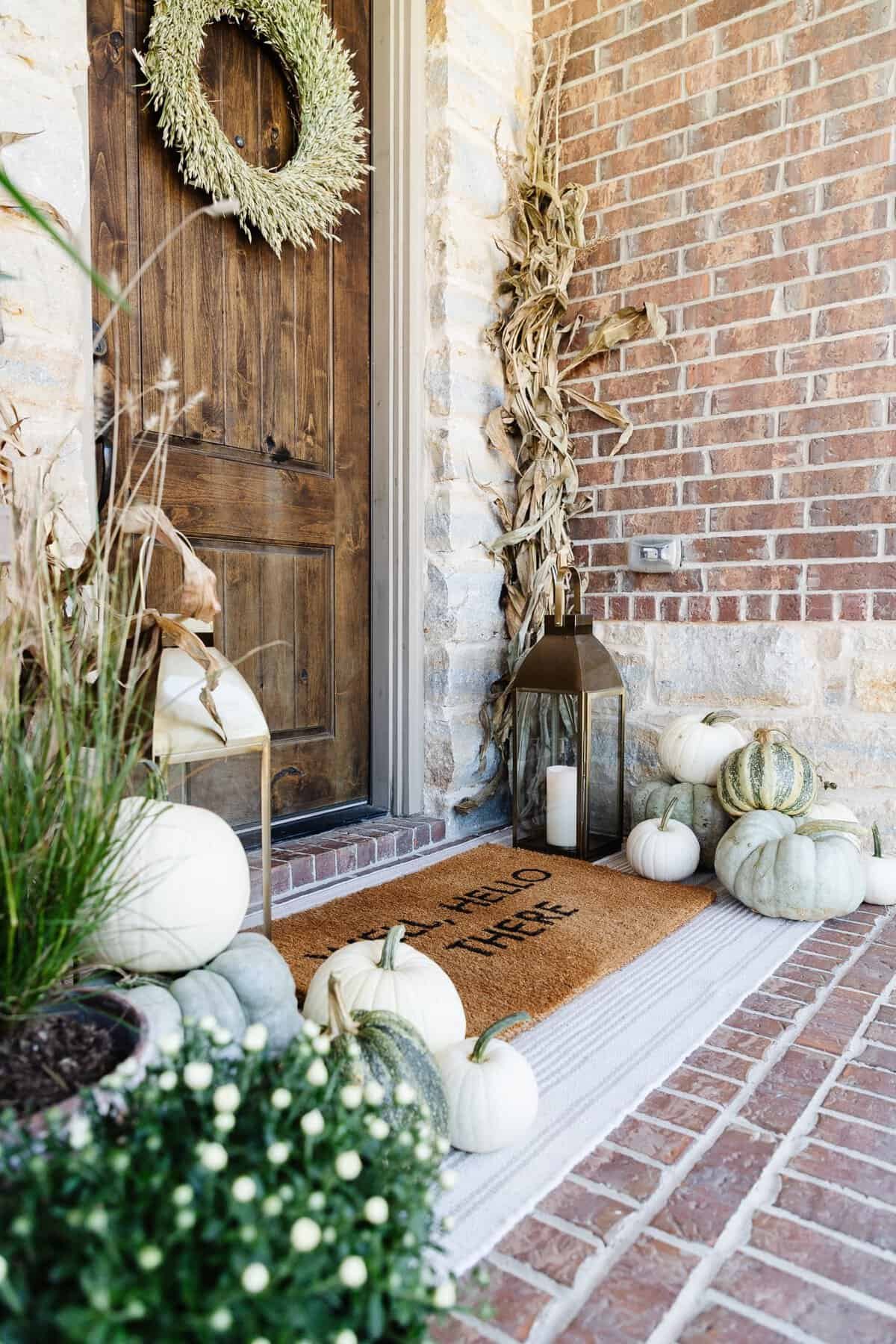 Neutral toned fall porch with upright cornstalk bundles, striped green pumpkins and lanterns