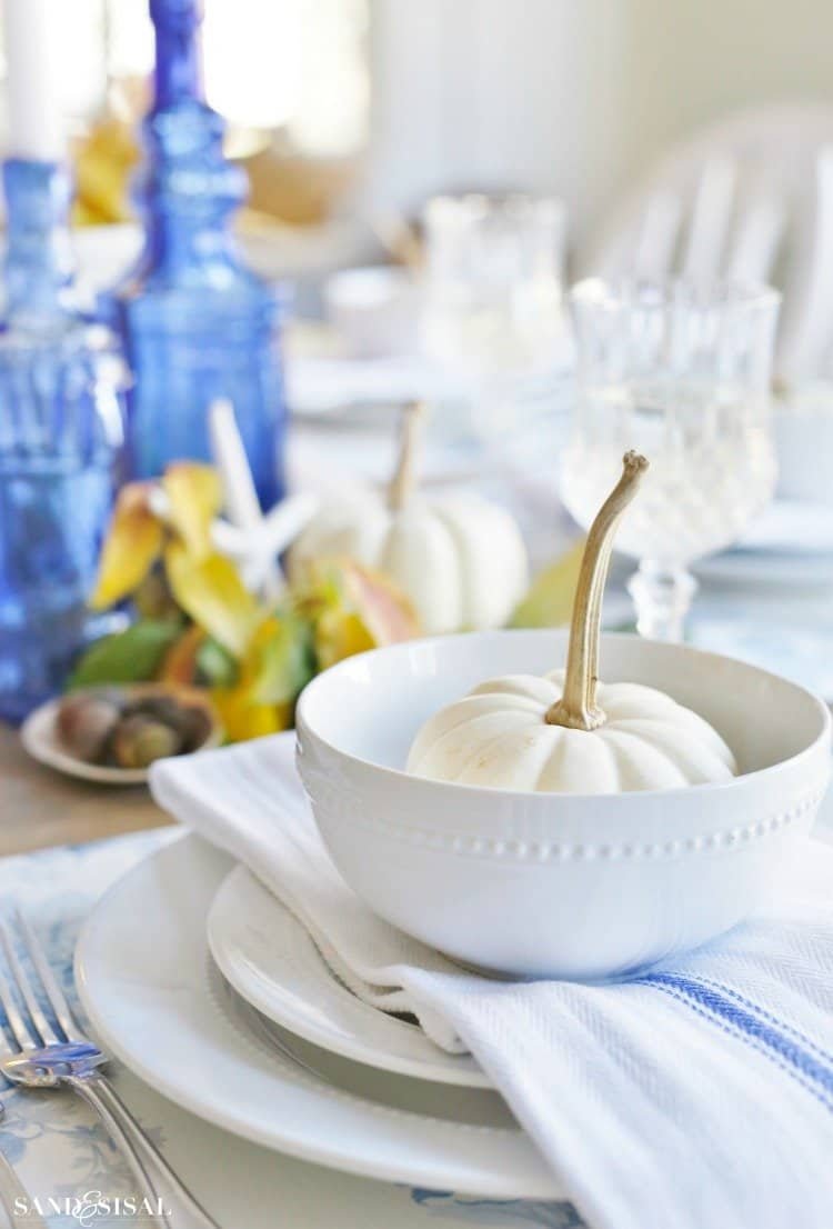 Coastal blue and white Thanksgiving table with white pumpkins, shells and cobalt bottles