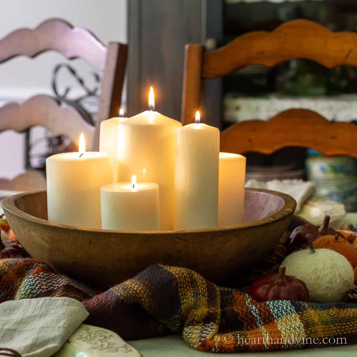 Antique dough bowl centerpiece with pillar candles, a plaid scarf and pumpkins