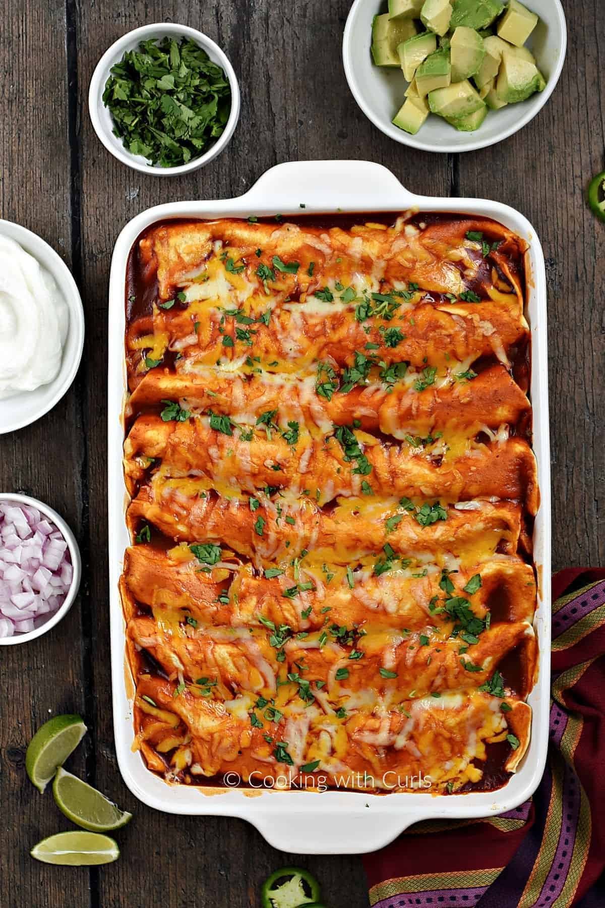 Pan of cheesy leftover turkey enchiladas with sour cream, red onion, cilantro and avocado